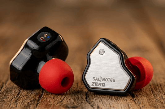 Salnotes Zero in-ear monitors with metallic faceplate and red ear tips on wooden surface.