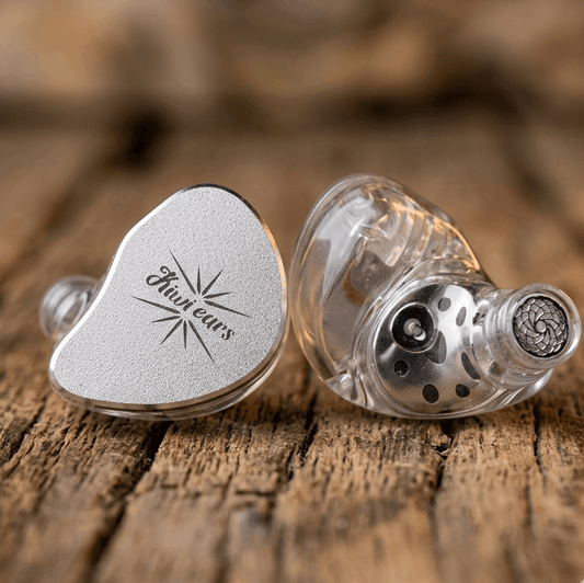 Kiwi Ears Belle custom in-ear monitors with silver faceplate and clear shell showing internal components on wood surface