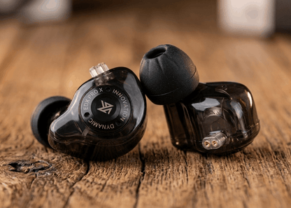 KZ EDX PRO X in-ear monitors with transparent housing and black ear tips, displayed on a wooden surface.