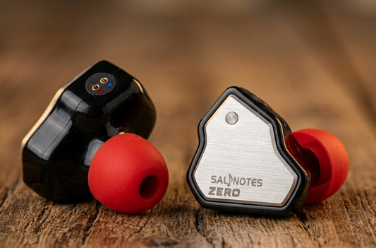 Salnotes Zero in-ear monitors with metallic faceplate and red ear tips on wooden surface.