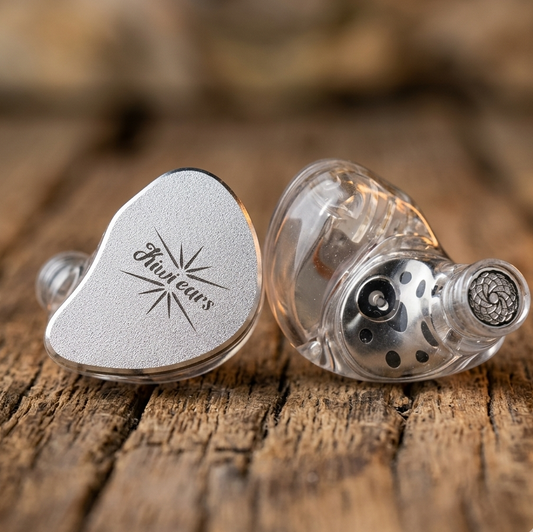 Kiwi Ears Belle custom in-ear monitors with silver faceplate and clear shell showing internal components on wood surface