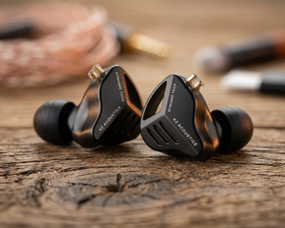 KZ ZVX in-ear monitors with dynamic drivers, featuring a sleek black design and ear tips, resting on a wooden surface.
