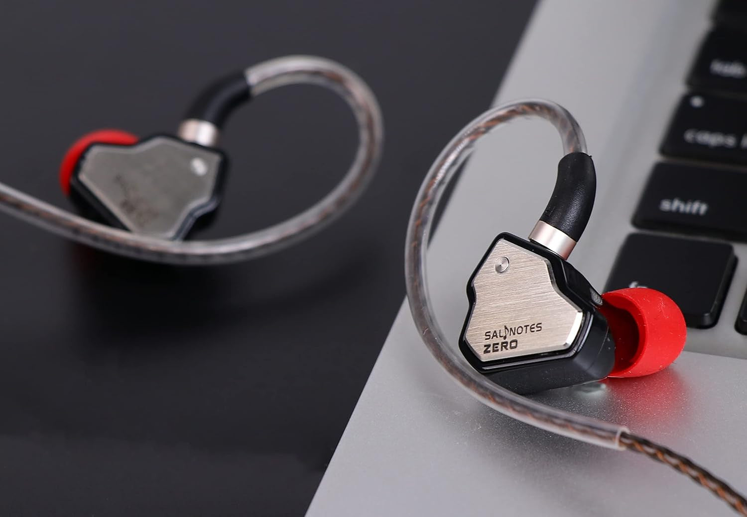 Salnotes Zero in-ear monitors with red earbuds and transparent cables placed near a laptop keyboard.